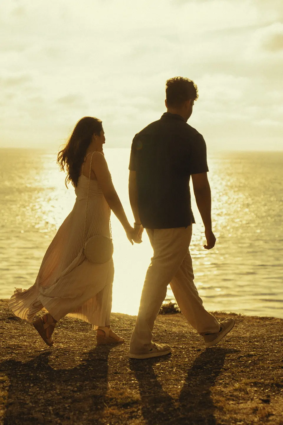 Rakshana and Nihal walking hand in hand along the shore at sunset.